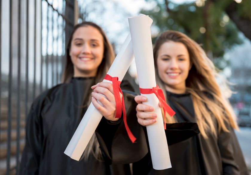 Duas mulheres comemorando a conquista de seus diplomas de MBA ou pós-graduação.