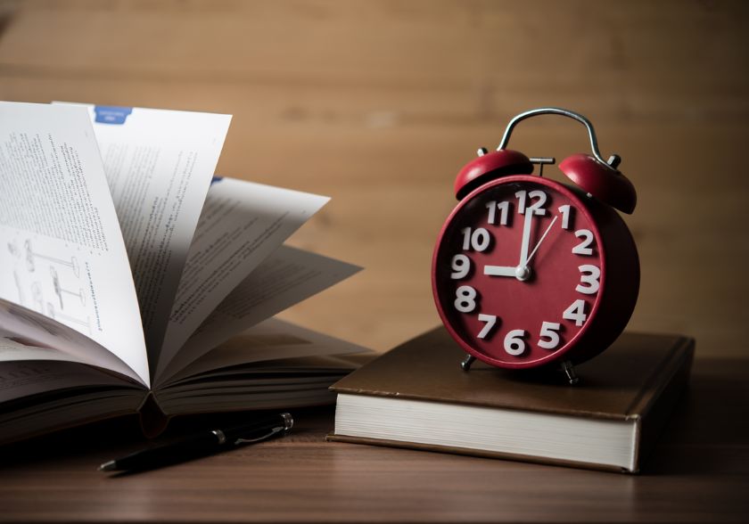 Relógio e livros sobre a mesa, ilustrando o uso do método Pomodoro no plano de estudos.