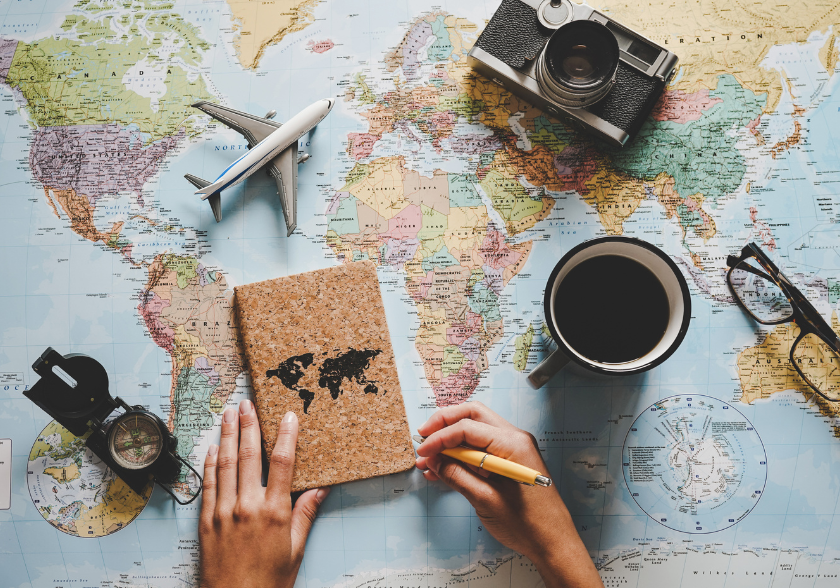 Mapa-múndi com caderno, avião e objetos de viagem representando educação além dos livros e liberdade para planejar a vida.